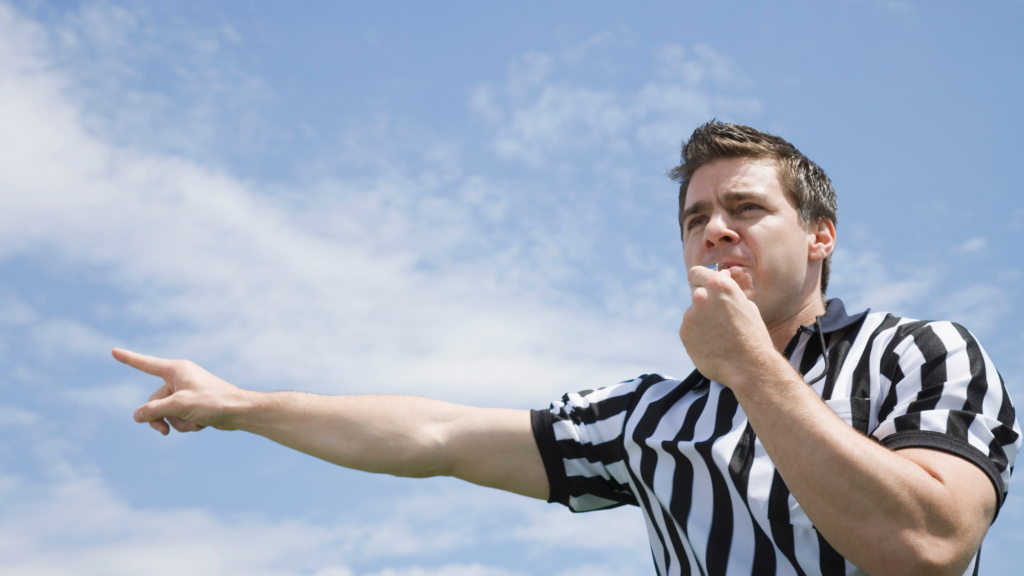 Whistleblowing: a referee in a black and white striped shirt blowing a whistle and pointing, against a blue sky